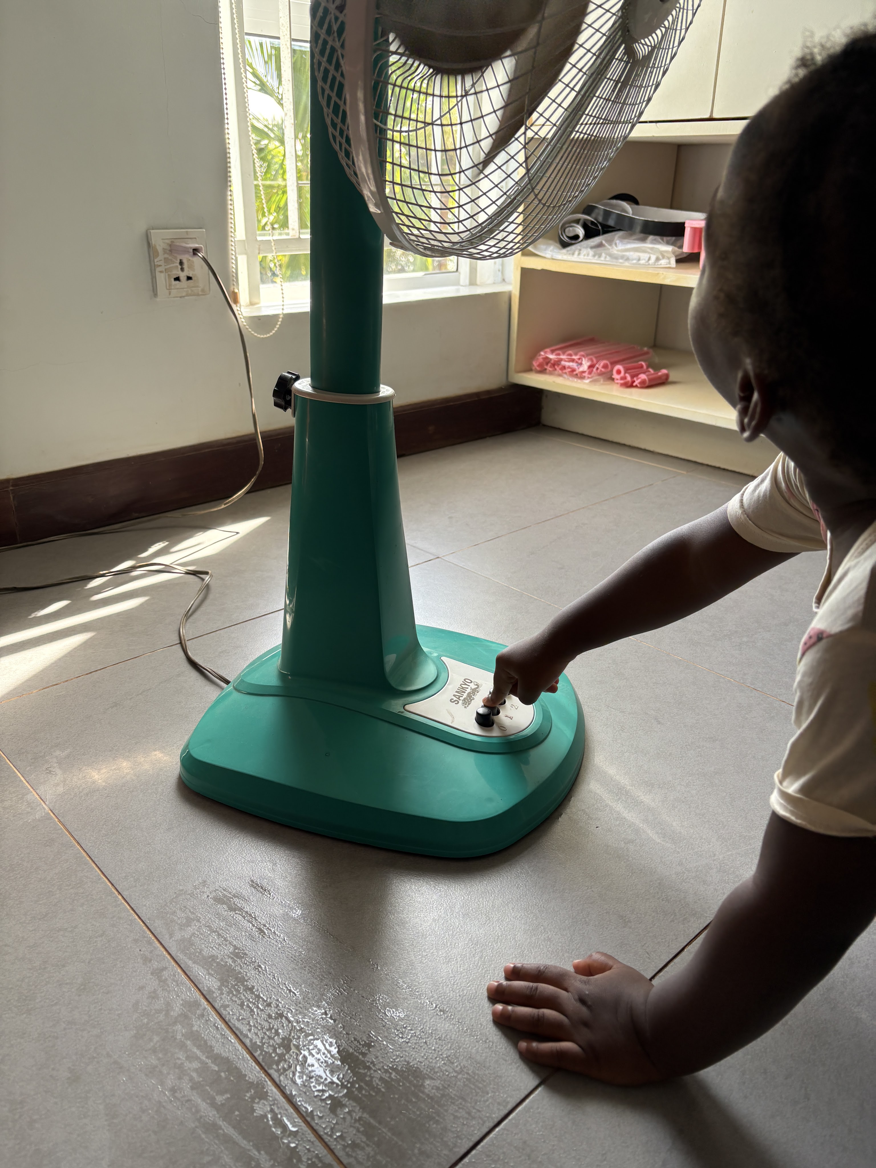 Small child pressing a button on a floor fan and looking up at the blades intently. From homegrownthinking.com